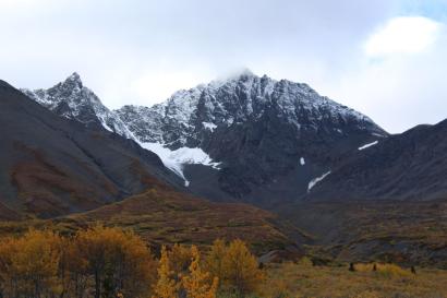 Auf den Bergspitzen liegt Schnee und ein Gletscher lugt zwischen zwei Bergen ein bisschen hervor.